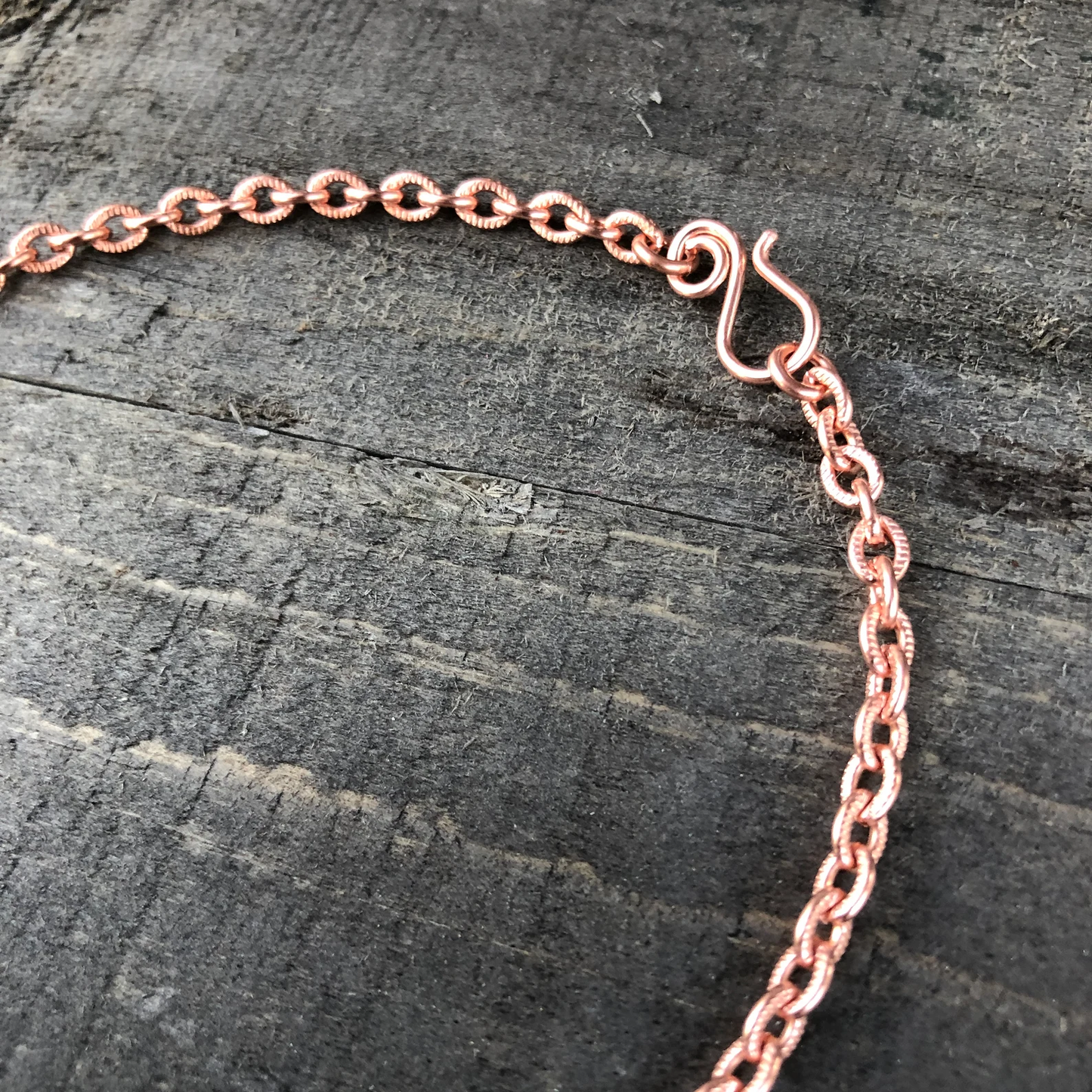 Rose gold chain necklace on a dark wooden surface